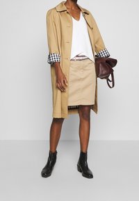Gabán beige con puños a cuadros en blanco y negro, parte superior blanca con escote en V, falda beige, botas negras de tobillo y bolso burdeos.