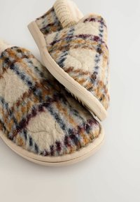 Pantoufles en laine avec une base crème ornée de motifs multicolores en carreaux bleus, bruns et bordeaux ; surface texturée et semelles beige.