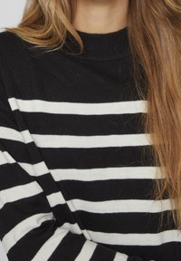 Randig svartvit tröja med hög krage, ribbat mönster och jämna horisontella ränder, delvis synliga hårstrån.