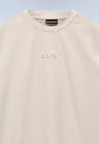 Lichtbeige katoenen t-shirt met een ronde hals, voorzien van een reliëf "NAPA" logo op de voorkant, een gladde textuur en een minimalistisch ontwerp.