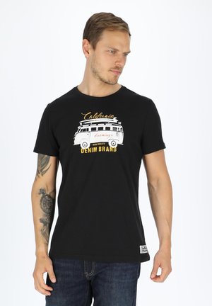 Schwarz Baumwoll-T-Shirt mit Rundhalsausschnitt, mit einem weißen Vintage-Van-Graphic und Text in Gelb und Weiß, kombiniert mit blauen Jeans.