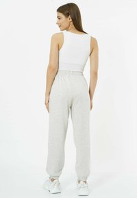 Hellgraue Baumwollsweatpants mit lockerer Passform, elastischem Bund und elastischen Bündchen, kombiniert mit einem weißen ärmellosen Oberteil.