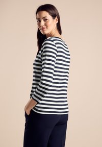 Pruhovaná košile s dlouhým rukávem v námořnické modři a bílé. Měkká textura, kulatý výstřih a přiléhavý střih. Spárována s tmavými kalhotami.