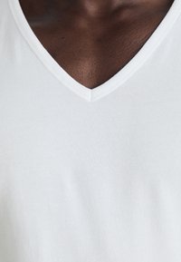 T-shirt en coton blanc à col en V avec une texture lisse et légère. L'encolure est bien définie, soulignant la simplicité du design.