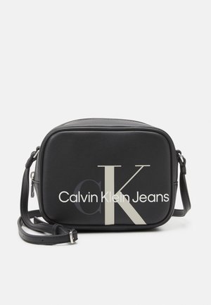 Sac banane rectangulaire noir avec bandoulière réglable, grand logo "ck" et texte "Calvin Klein Jeans" sur le devant.