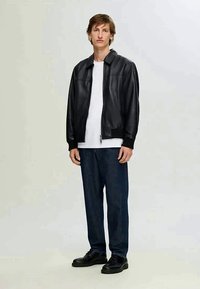 Melna ādas jaka ar rāvējslēdzēju priekšpuses, ribotām piedurknēm un apkakles kakla izgriezumu, uzvilkta virs baltas T-kreklas un tumšajiem džinsiem. Melni apavi noslēdz izskatu.