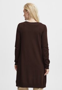 Długi brązowy sweter z dzianiny z okrągłym dekoltem, długimi rękawami i prążkowanymi mankietami, z bocznymi rozcięciami ułatwiającymi ruch.