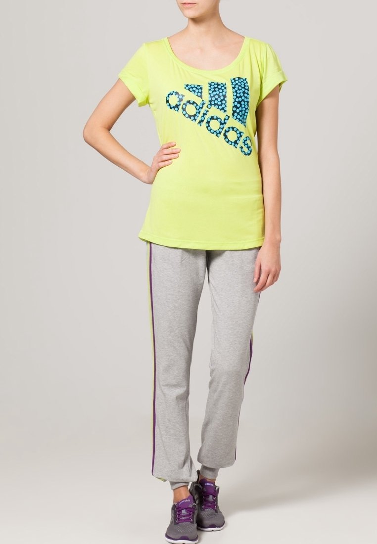 Neongul t-shirt med blå prickig Adidas-logotyp, matchad med grå byxor med lila sidostripes. Bekväma sportkläder och sneakers.