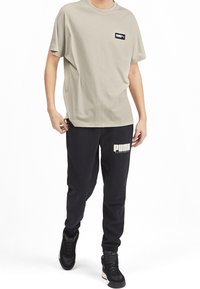 Světle šedé bavlněné tričko s krátkým rukávem a černou nášivkou loga, doplněné černými tepláky s bílým potiskem "PUMA". Černé tenisky.