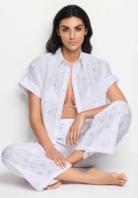 Completo di cotone bianco con una camicia a maniche corte con ricami ad occhio e pantaloni abbinati dalla vestibilità ampia. I dettagli includono motivi floreali ritagliati.