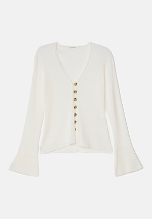 Λευκό ριπ πλεκτό κάρντιγκαν με μακριές φουσκωτές μανίκες, V-λαιμό και έξι καφέ κουμπιά μπροστά.
