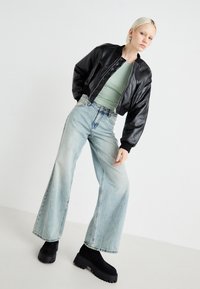 Černá zkrácená kožená bomber bunda, mintově zelený upnutý top, široké světlé modré džíny a robustní černé platformové boty. Hladká textura po celém povrchu.