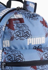 Blå tygryggsäck med graffiti-stil text och grafik, med en framficka med dragkedja och justerbara remmar. Puma-logotypen visas framträdande.