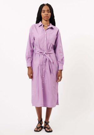 Lichtpaarse button-up jurk met lange mouwen, een riem in de taille en een borstzak. De textuur lijkt glad; knielang met zijslits.