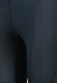 Musta legginsit, joissa on sileä pinta, tiukka istuvuus ja vahvistetut saumat sivuilla lisäämään kestävyyttä ja rakennetta.