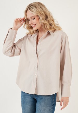 Light beige button-up shirt, long sleeves, relaxed fit, classic collar, smooth texture, paired with blue jeans. No patterns or notable accents.