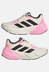 Des chaussures avec une tige en maille blanche, des rayures noires et un col rembourré. Accent marqué de rose sur la semelle intermédiaire et une semelle texturée pour une meilleure adhérence.