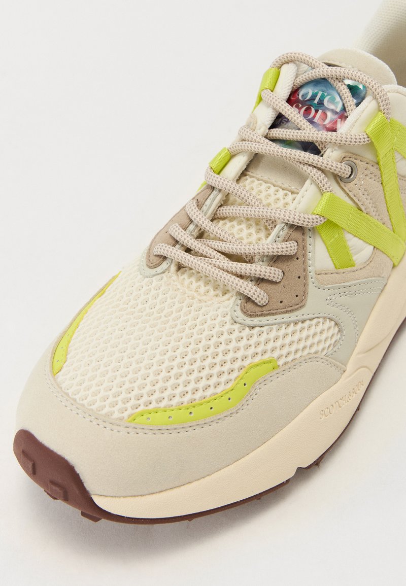 Baskets avec un upper en mesh beige, des accents verts, une semelle marron et des détails en cuir suédé texturé. Présente un logo multicolore sur la languette.