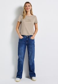 Camiseta beige con el texto "easy going", combinada con jeans azules. Los jeans son de corte holgado y se llevan con zapatillas blancas.