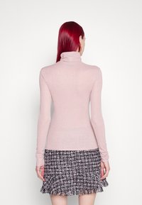 Helles rosa Langarm-Turtleneck-Oberteil mit figurbetontem Schnitt, aus einem strukturierten Material gefertigt, kombiniert mit einem schwarz-weißen, fransigen Tweed-Rock.