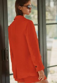 Rød linnedblazer med et struktureret design, notch-krave, enkelt knapdetalje og sideslidser. Sammen med matchende shorts.
