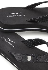 Black flip-flops with textured straps, featuring a shiny black accent, white logo, and white side detailing. Soft foam sole for comfort.