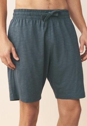 Homme portant un short de sport gris foncé à mi-cuisse avec taille élastique et cordon, les mains reposant sur les côtés.