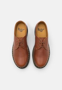 Brūni ādas šaura apavi ar noapaļotu pirkstu, ar dzeltenu vīšanu uz melna gumijas zoles un gludu tekstūru.