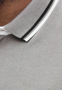 Close-up van de grijze, gestructureerde kraag van een polo shirt met zwart-witte strepen, gedragen door een persoon met een donkere huid.