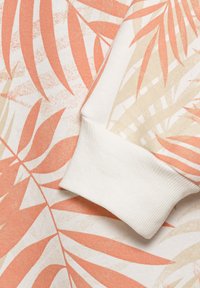 Maglione di cotone con un motivo di foglie di palma color pesca e beige. Il polsino bianco a coste, la texture morbida e i dettagli arancioni creano un design stratificato.