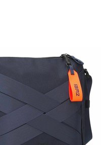 Borsa a tracolla in tessuto blu navy, caratterizzata da un motivo geometrico con cinghie incrociate, zip nera e un etichetta arancione con la scritta "iam2."