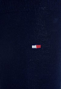 Calcetines azul marino con textura acanalada presentan un pequeño logo bordado en rojo, blanco y azul. Diseño sencillo y ajuste regular.