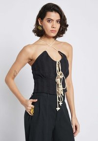 Top nero in maglia con scollo all'americana, caratterizzato da un dettaglio a taglio e un cordoncino color crema. Il tessuto testurizzato aggiunge interesse visivo.