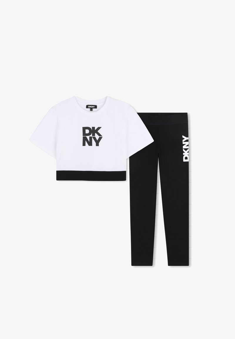 Biały krótki t-shirt z czarnym logo DKNY i czarną lamówką; zestawiony z czarnymi legginsami z białym logo DKNY po bokach.