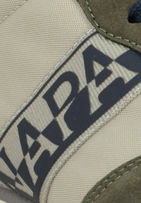 Zapatilla beige con un logo azul marino que dice "NAPA," acentuada con ante verde cerca del talón y tejido texturizado en toda la superficie.