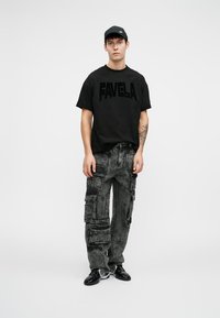 Svart bomulls t-skjorte med "FAVELA" trykt i fet skrift, sammen med mørkegrå cargo-bukser med flere lommer og en teksturert finish. Svart sneakers.