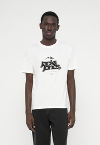 Λευκό βαμβακερό t-shirt με έντονο μαύρο λογότυπο και γραφικά βουνού. Βραχία μανίκια και στρογγυλή λαιμόκοψη. Φοριέται με σκούρα τζιν.