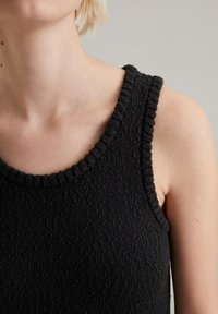 Zwarte mouwloze top met een gestructureerd breipatroon, voorzien van een ronde halslijn met een ribbelrand en gladde randen. Aangepaste pasvorm.
