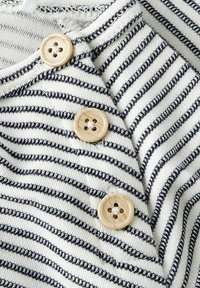 Gros plan sur un tissu crème à rayures horizontales noires avec trois boutons ronds en bois clair cousus en rangée verticale.