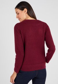 Maglione bordeaux con una trama texturizzata, scollatura rotonda e maniche lunghe. L'orlo si ferma all'altezza dei fianchi, mettendo in evidenza una silhoutte aderente.