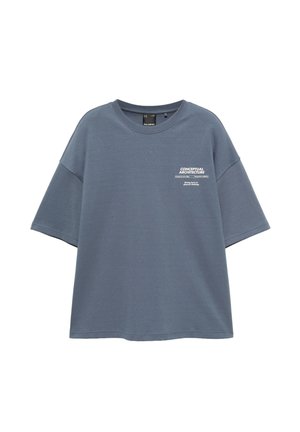 T-shirt bleu oversize à manches courtes avec le texte "CONCEPTUAL ARCHITECTURE" et un petit graphique sur la partie gauche de la poitrine.
