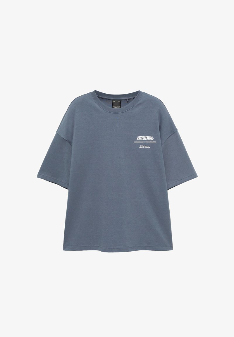 T-shirt bleu oversize à manches courtes avec le texte "CONCEPTUAL ARCHITECTURE" et un petit graphique sur la partie gauche de la poitrine.
