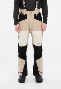 Beige en zwarte skibroek met patchzakken, verstelbare banden en een waterafstotende afwerking. Heeft een logo op het bovenbeen.