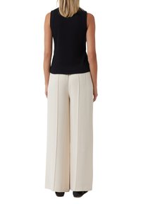 Schwarzes ärmelloses Top, kombiniert mit cremefarbenen, weit geschnittenen Hosen. Das Outfit zeichnet sich durch ein einfaches Design und eine glatte Stofftextur aus.