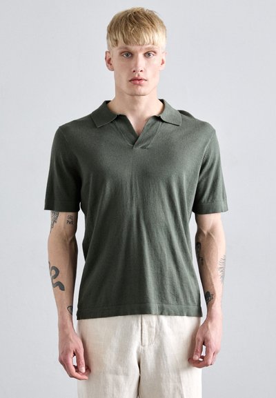 Polo de manga corta en verde oliva, hecho de suave tejido de punto. Presenta un cuello en V y un collar plano, con un corte relajado y sin patrones.