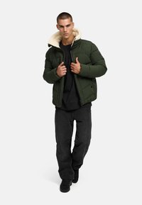 Žalias paminkštintas džemperis su kreminiu dirbtiniu kailiu, priekinis užtrauktukas ir dvi šoninės kišenės. Nešiojamas ant juodos marškinėlės ir suderintas su juodomis kelnėmis.