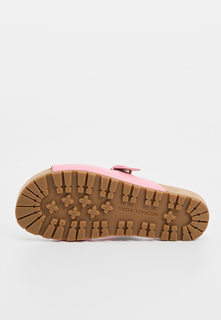 Semelle de sandale avec un motif de crantage profond en caoutchouc marron, bride supérieure rose avec boucle, et marque "MICHAEL KORS" sur la semelle.