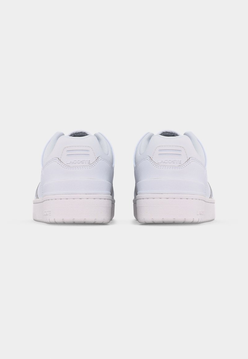 Een paar witte Lacoste sneakers gezien van achteren, met gestikte details en een gestructureerde zool tegen een effen achtergrond.