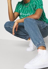 Grön t-shirt med vita linjer, ljusblå denimjoggers och vita sneakers. Joggers har elastiska muddar och sidofickor.