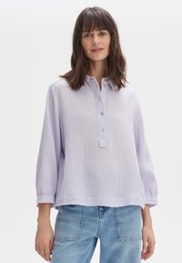 Maglione pullover lavanda chiaro con una finitura testurizzata e stropicciata, abbottonatura e maniche ampie e larghe, abbinato a jeans azzurri chiari.